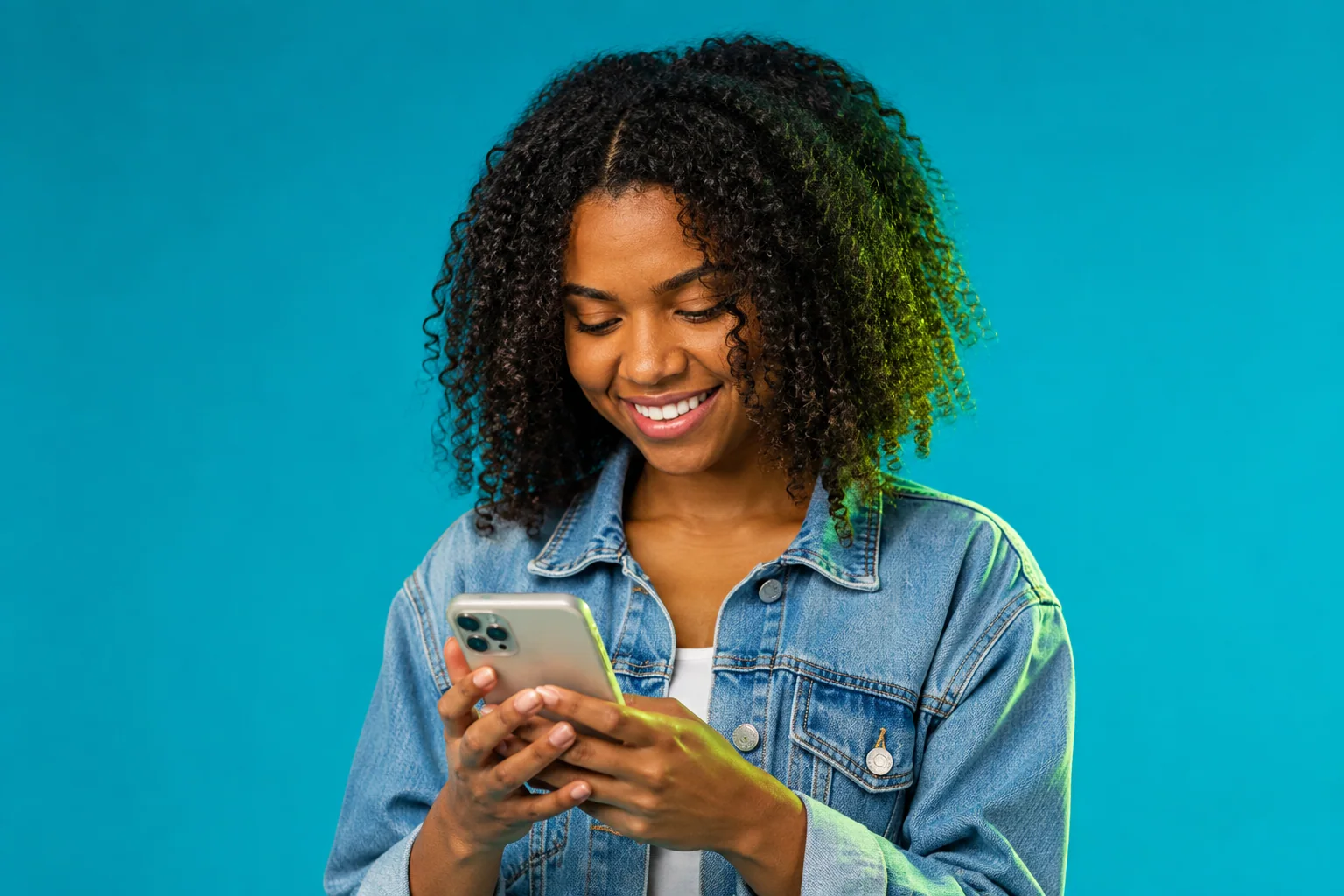 Jovem de cabelo cacheado usando o celular em um fundo turquesa.
